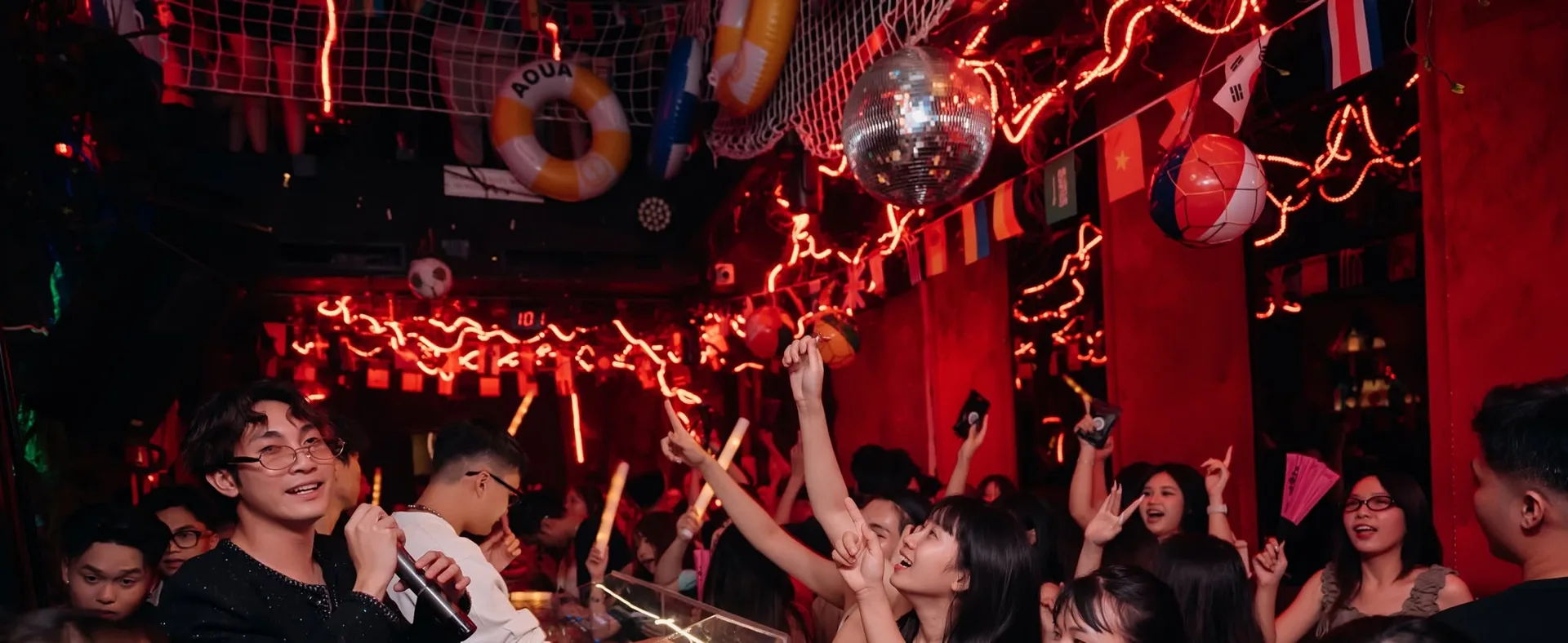 HYBRA Ultra Lounge — trần lưới treo phao, quả cầu disco và dây đèn đỏ uốn lượn