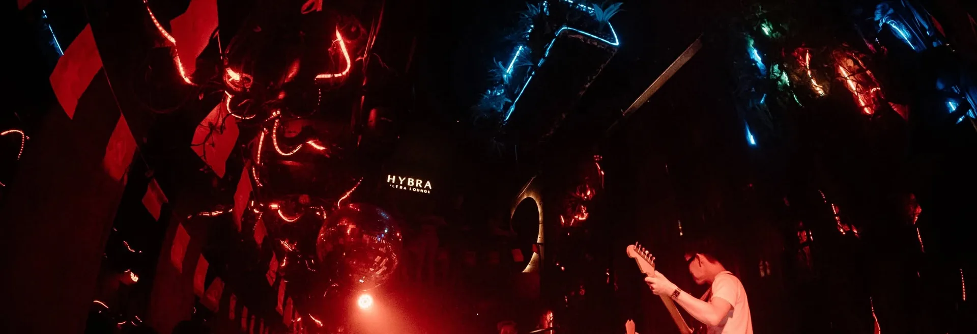 HYBRA Ultra Lounge — trần dây đèn đỏ, quả cầu disco và biển tên HYBRA sau sân khấu